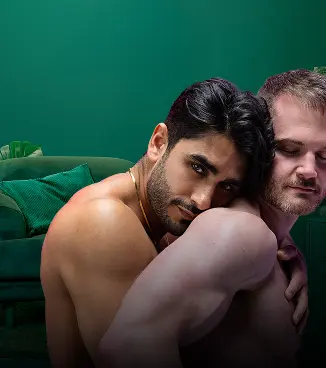 Two shirtless men embracing closely, one resting his head against the other's shoulder